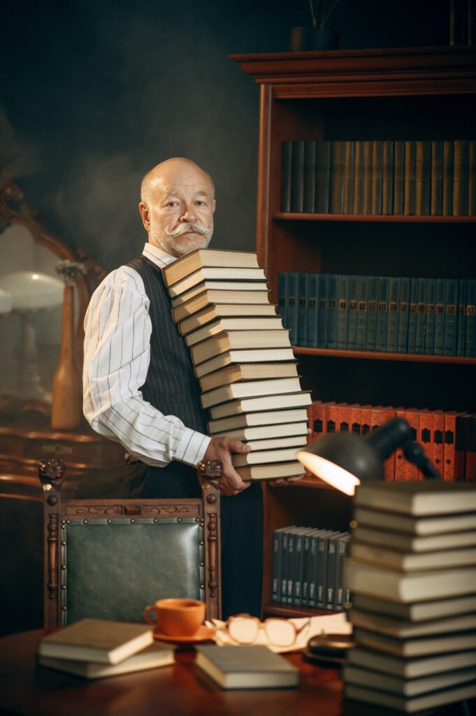 Elderly writer holds stack of books in home office